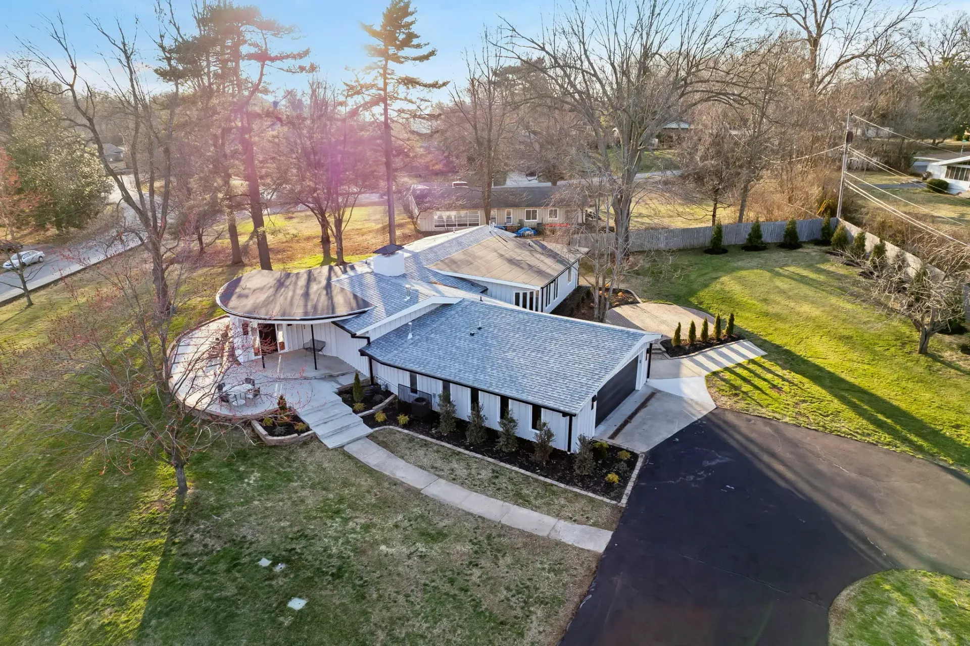 Aerial view of a white-roofed building with a curved walkway, surrounded by trees and a parking lot at sunset