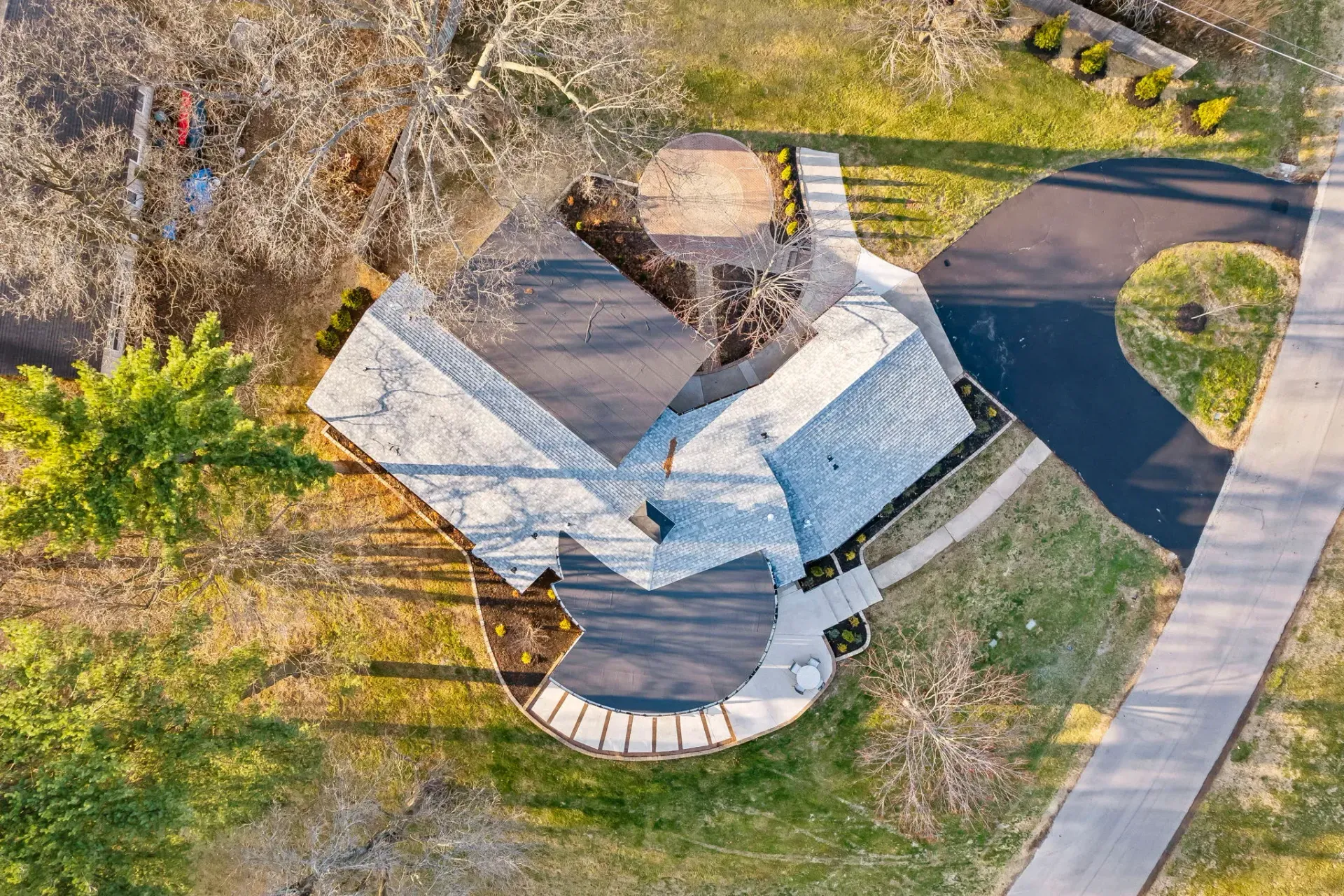 Aerial view of a small house with a gray roof beside a curved sidewalk and grassy yard