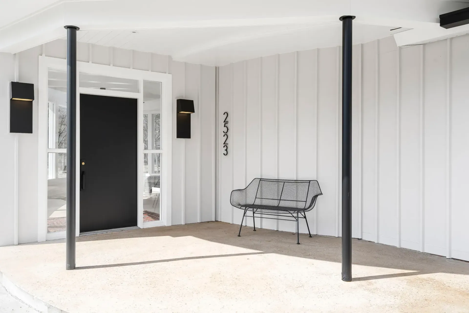 Covered patio with white paneled walls, black support posts, and a bench near an open doorway