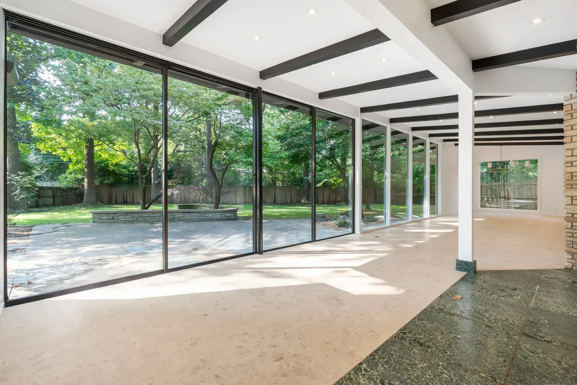 Bright empty hall with floor-to-ceiling glass walls, exposed beams, and sunlight on the floor looking onto greenery.