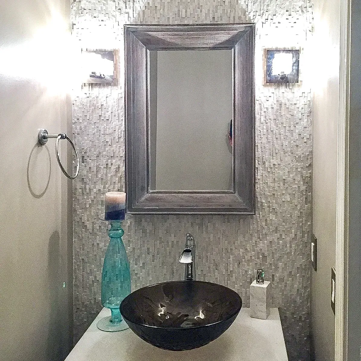 Small bathroom vanity with round black sink, mirror, wall lights, and blue soap dispenser