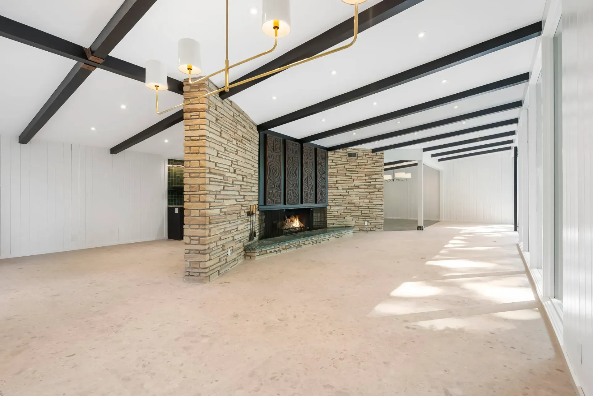 Spacious empty room with white walls, exposed beams, stone fireplace, and carpeted floor