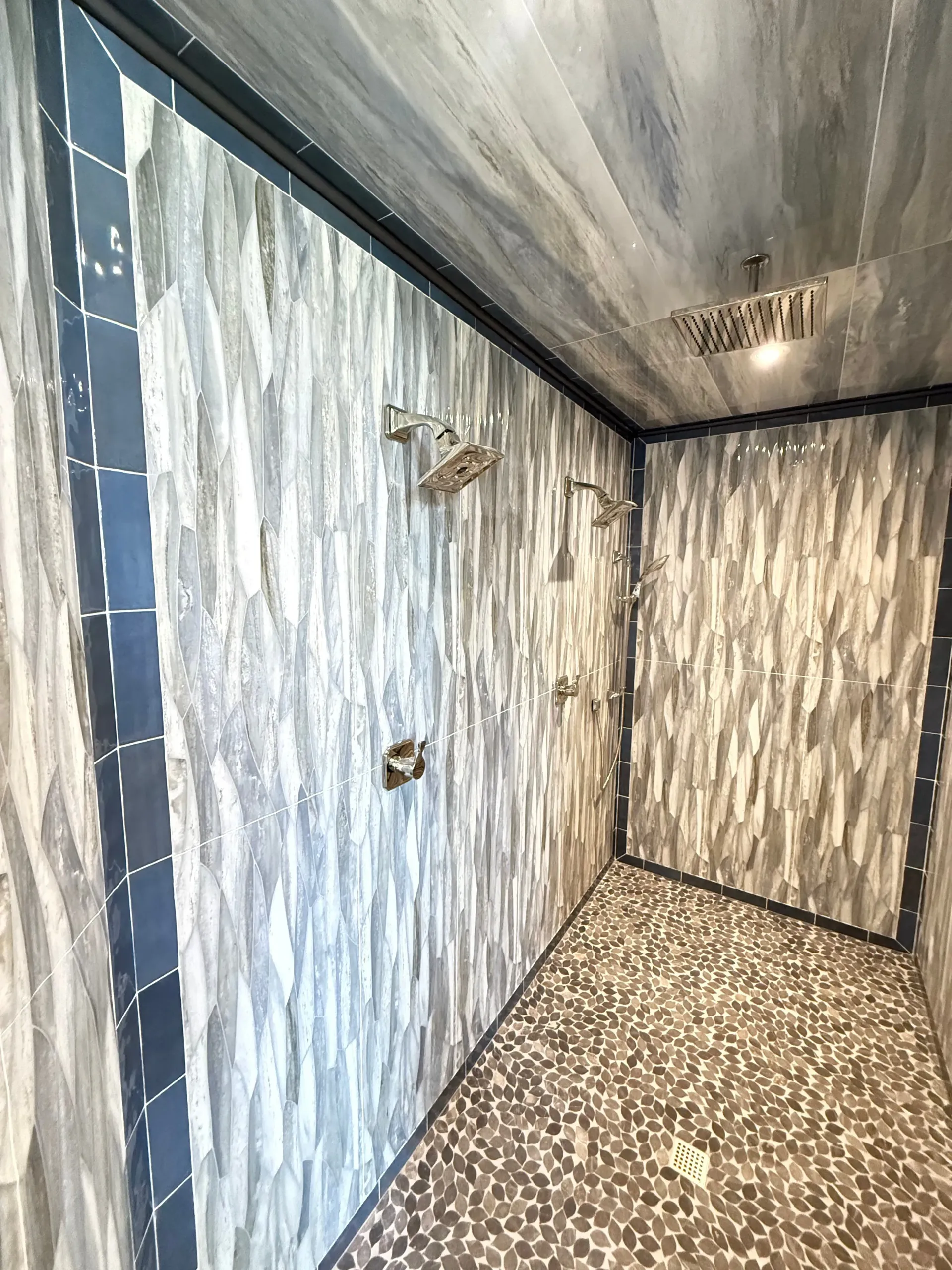 Marble-tiled walk-in shower with glass wall, chrome fixtures, and pebble floor
