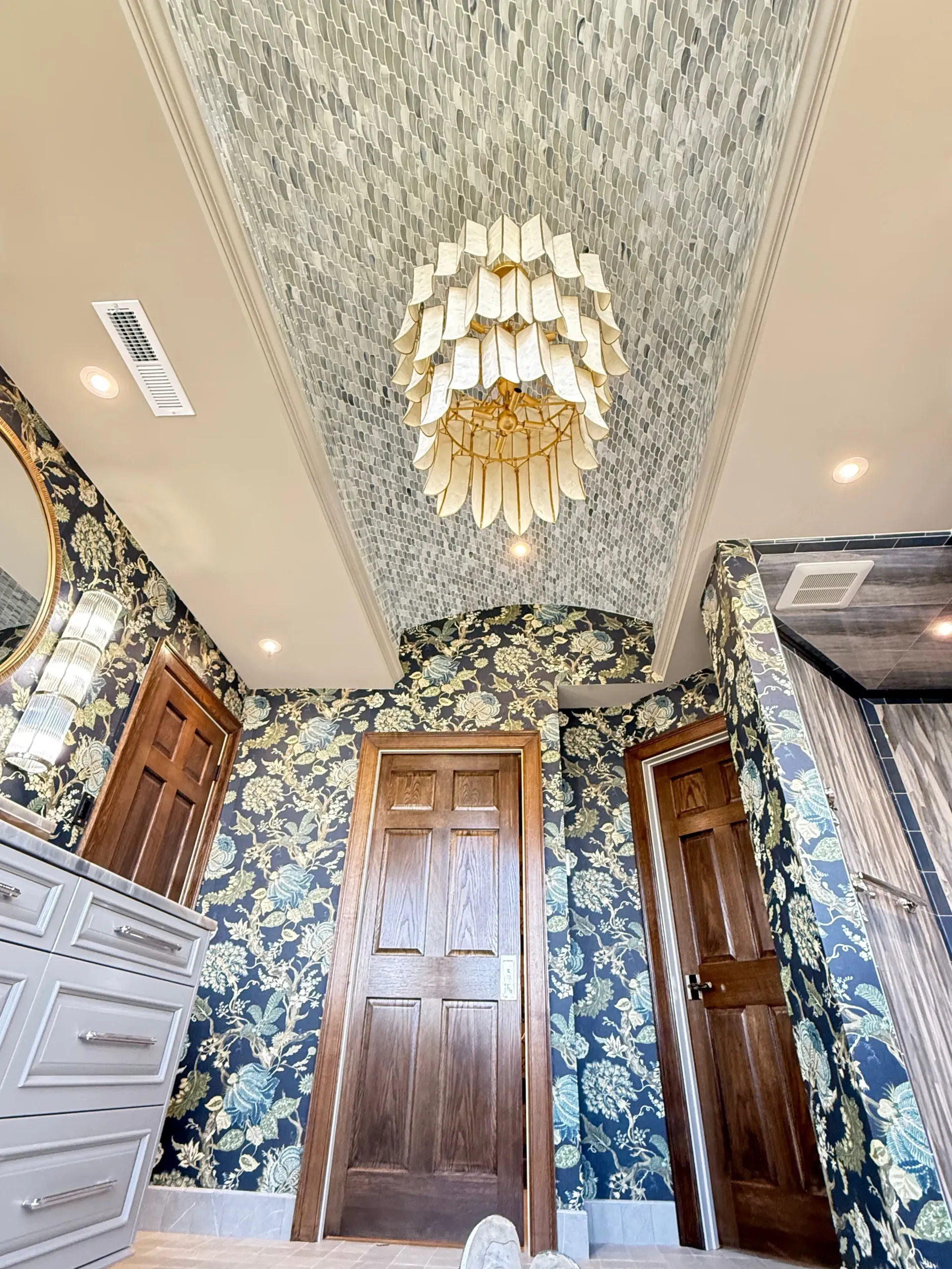 Elegant floral wallpapered hallway with wood doors, chandelier, and patterned ceiling