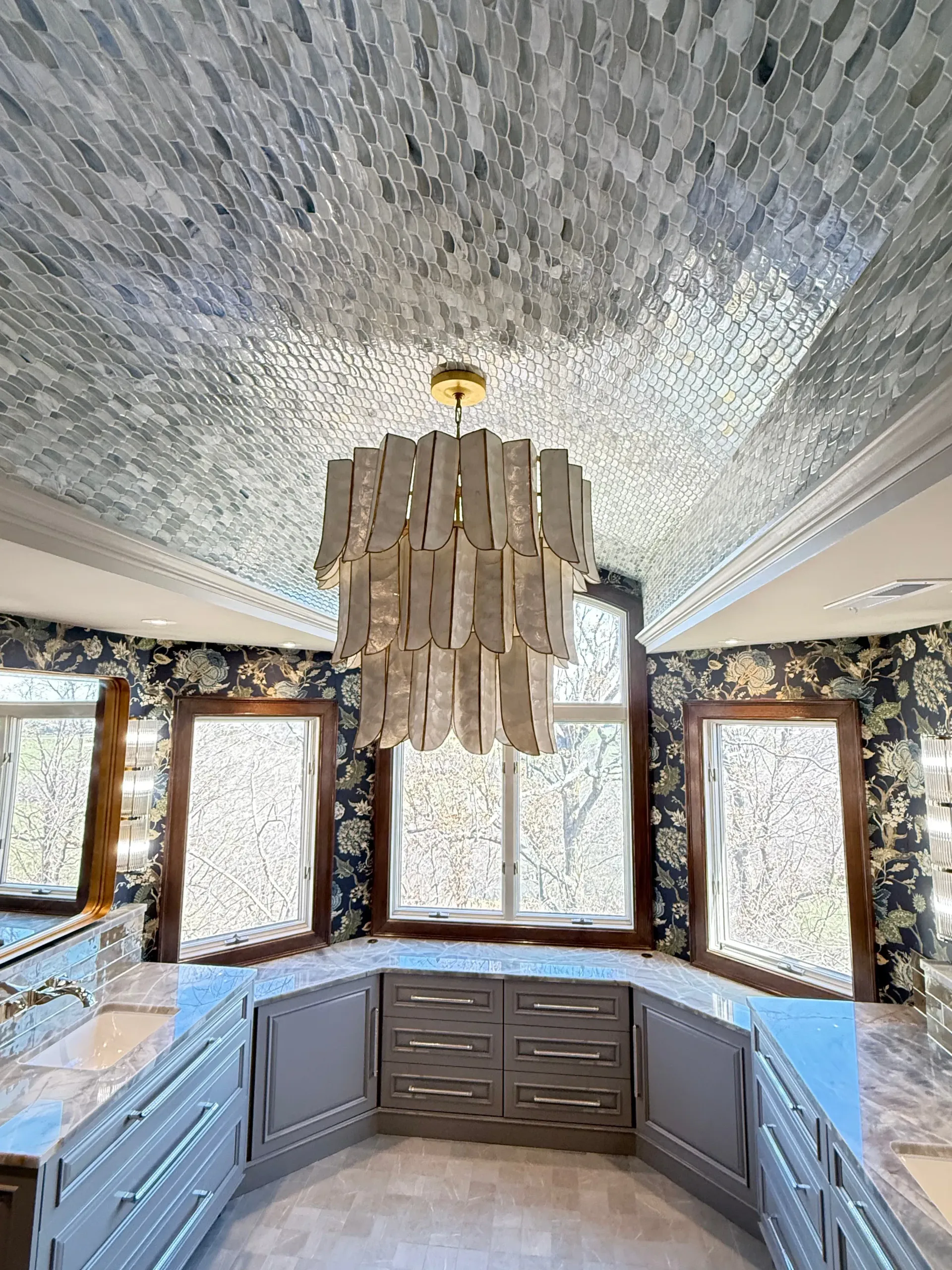 Elegant kitchen with a large chandelier, mosaic ceiling, patterned wallpaper, and white countertops.