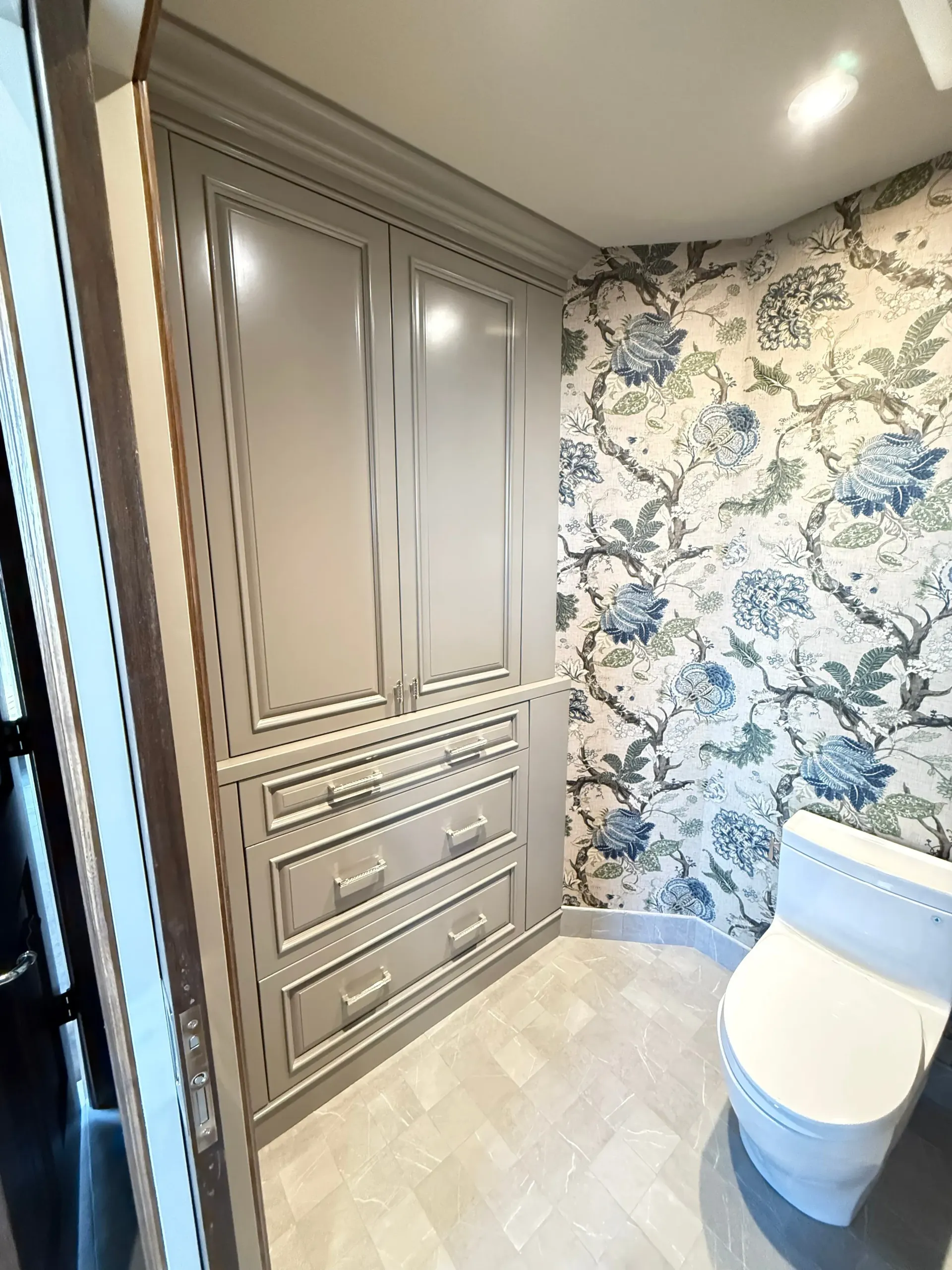 Small bathroom with floral wallpaper, built-in beige cabinets, and a white toilet.