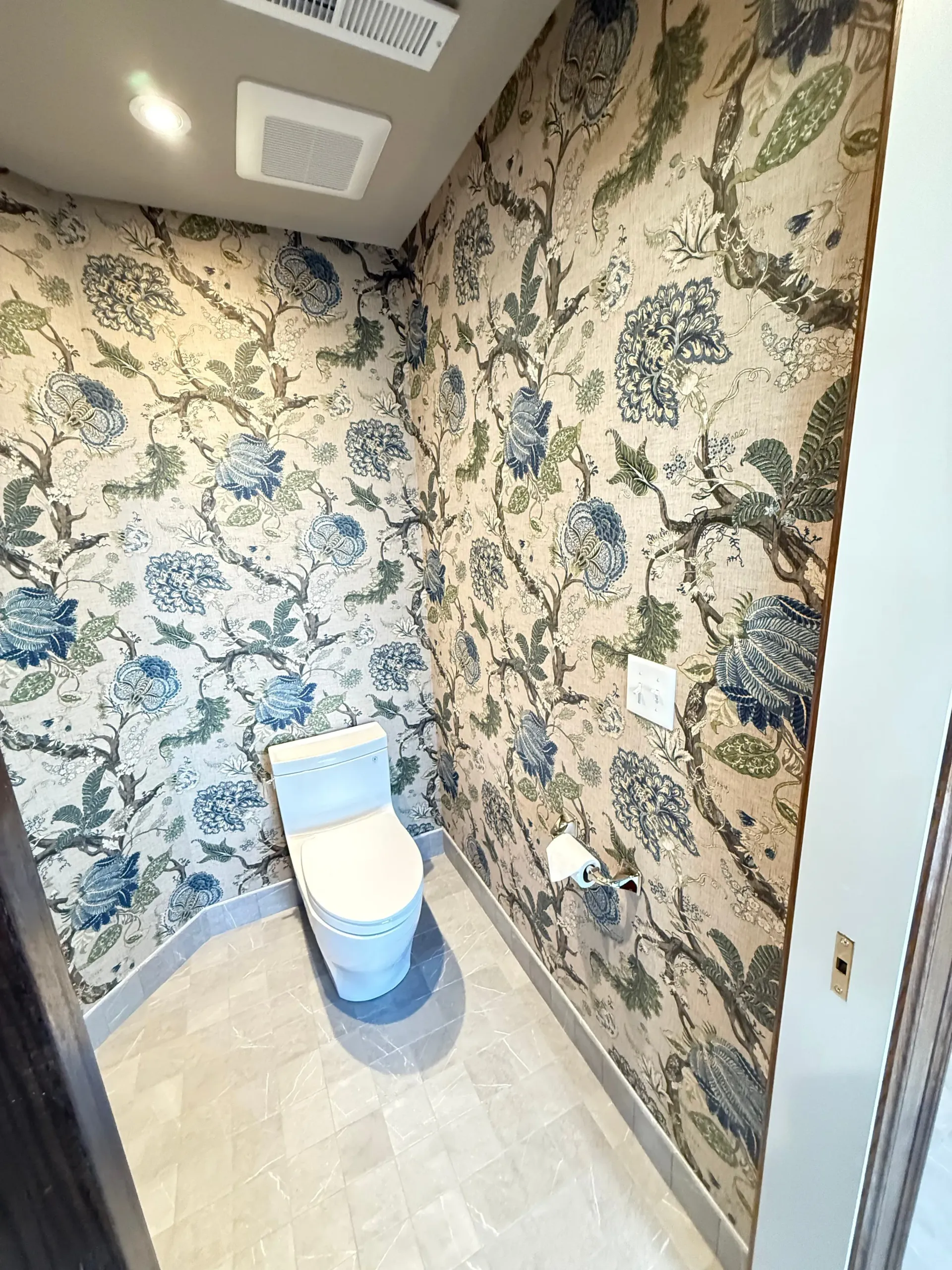Small bathroom with floral wallpaper, toilet, and light tile floor.