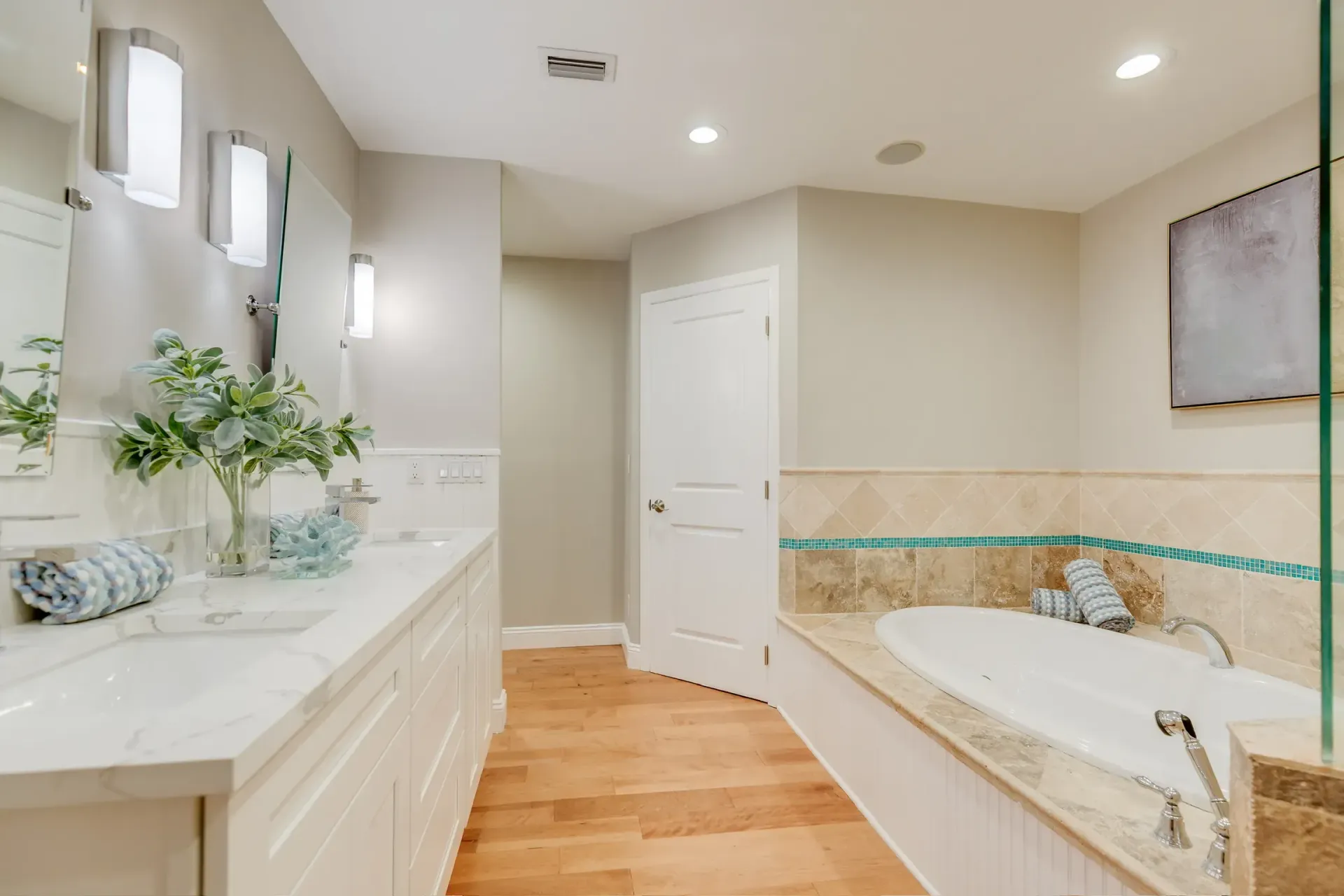 Bright bathroom with white vanity, freestanding tub, beige tile, and hardwood floor
