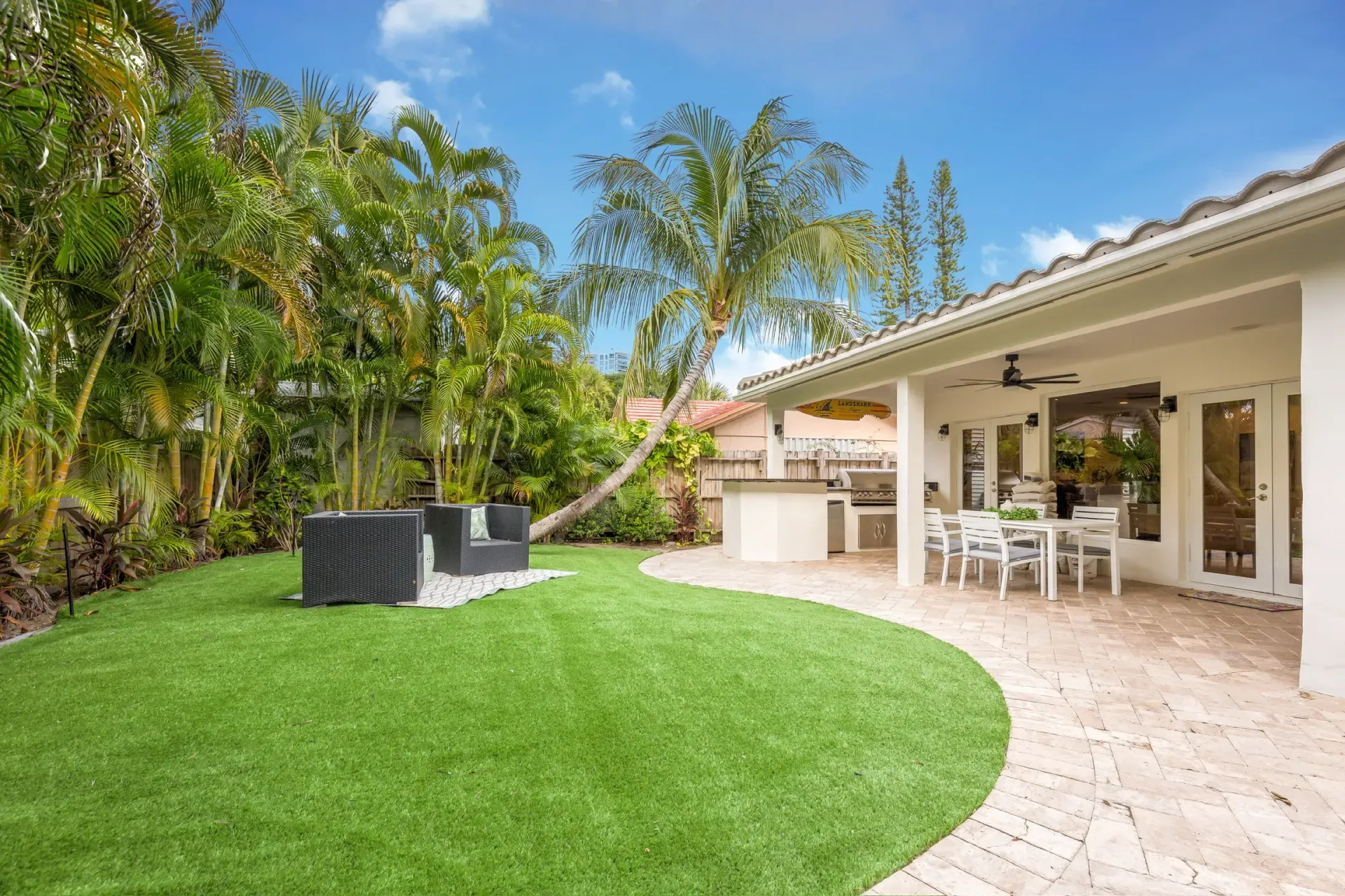 Backyard patio with green lawn, palm trees, and covered outdoor dining area