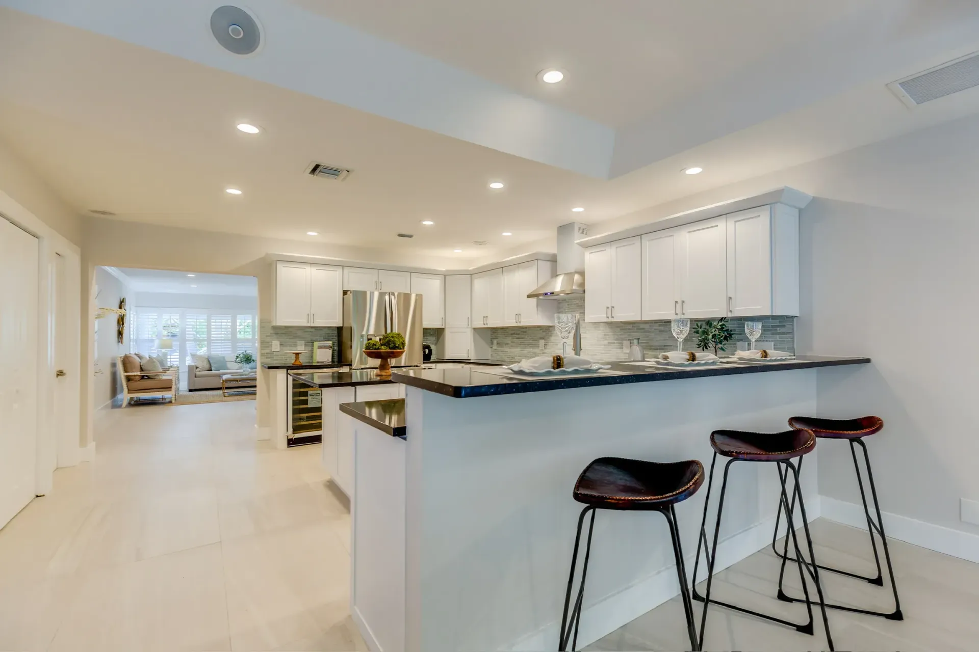 Bright modern open-plan kitchen with white cabinets, black counters, and two bar stools