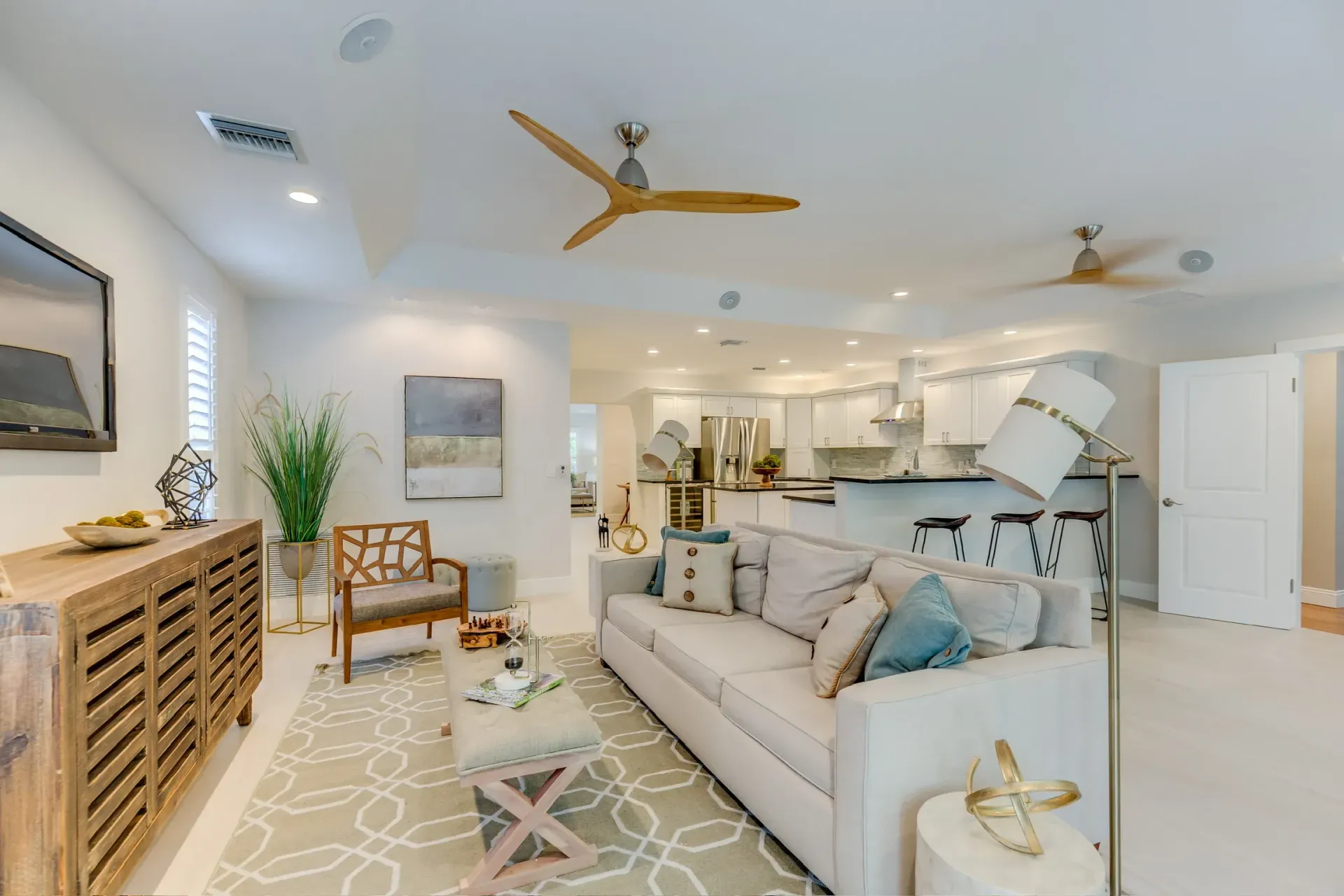 Bright airy living room with beige sofa, ceiling fans, white walls, and coastal decor