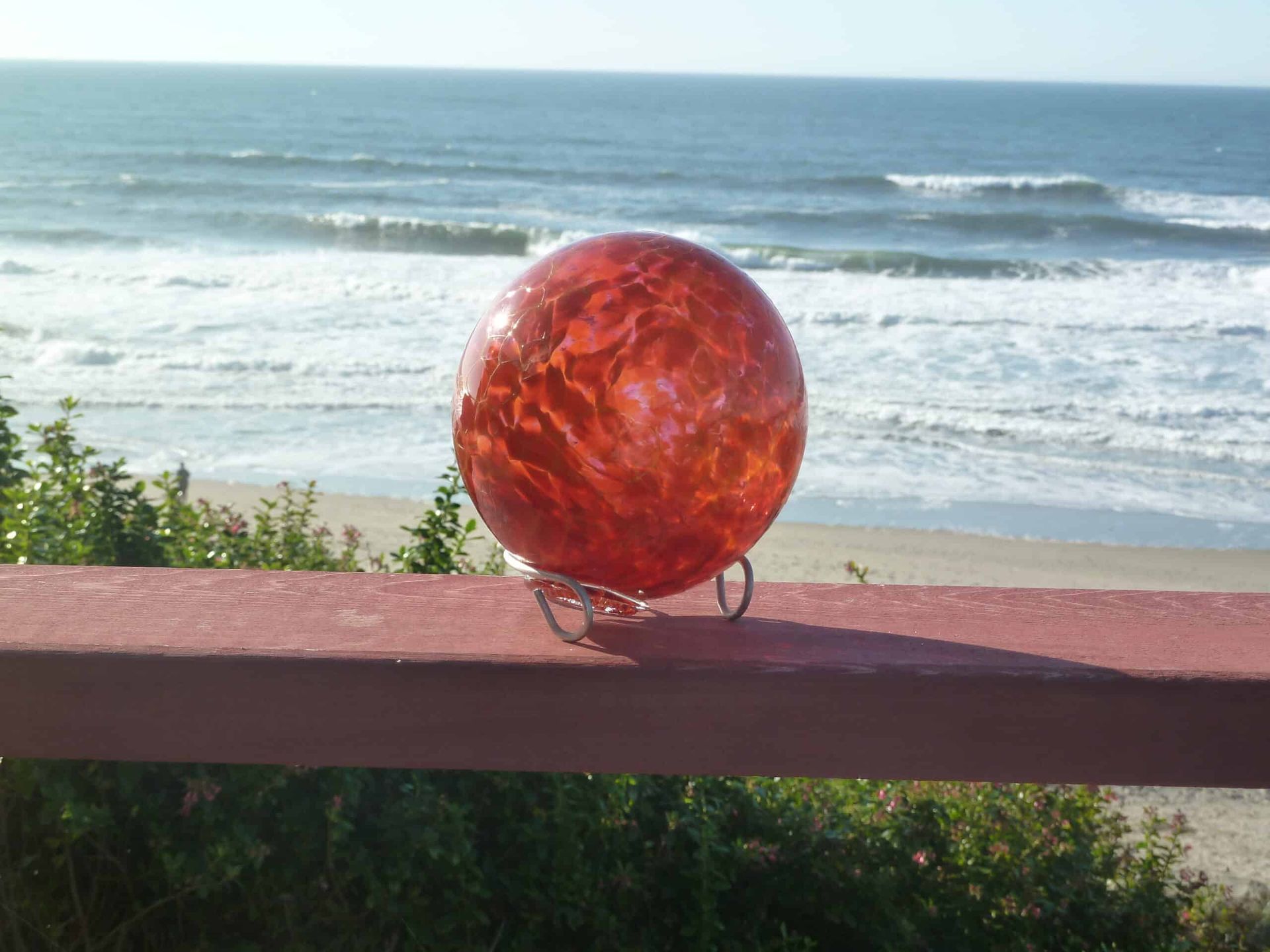 A red glass ball is sitting on a railing overlooking the ocean.