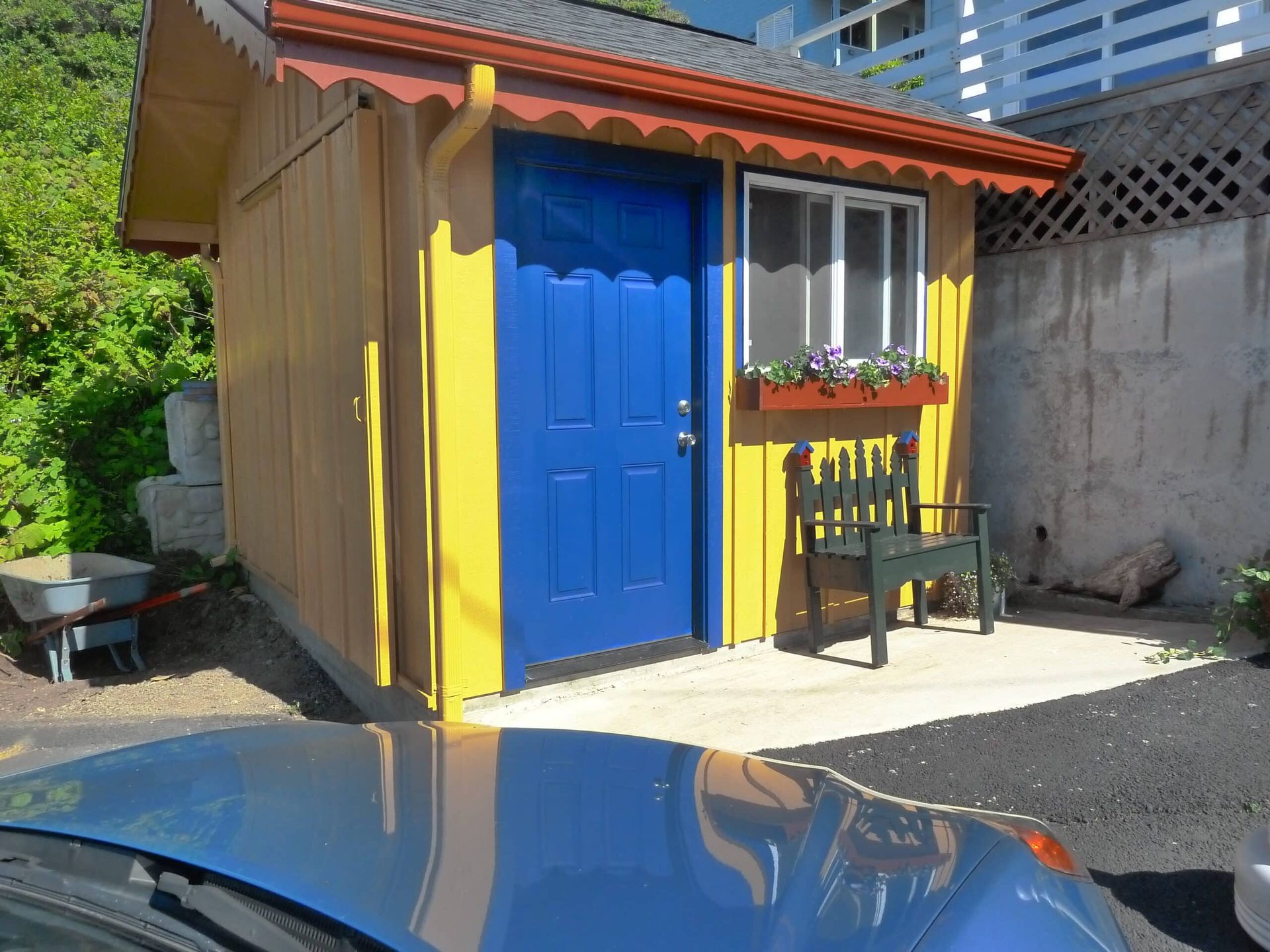 A blue car is parked in front of a yellow shed with a blue door