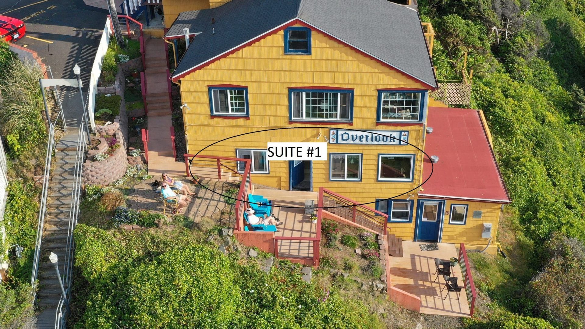 Aerial view of a yellow hillside house with a deck, patio furniture, and signs reading
