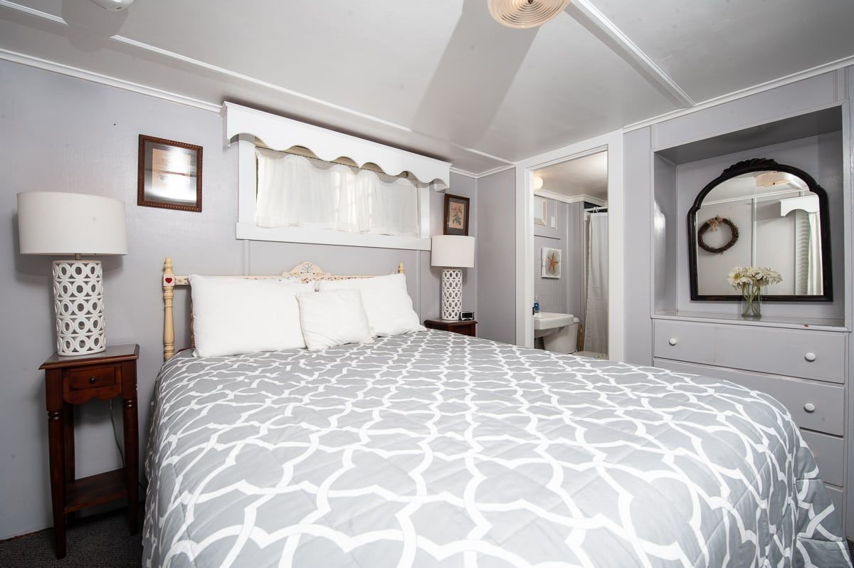 Bright bedroom with gray patterned bedding, white walls, and matching lamps and dresser.