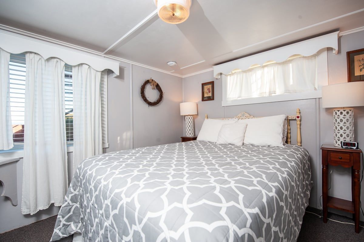 Bright bedroom with a large bed, gray patterned comforter, white curtains, and soft gray walls.
