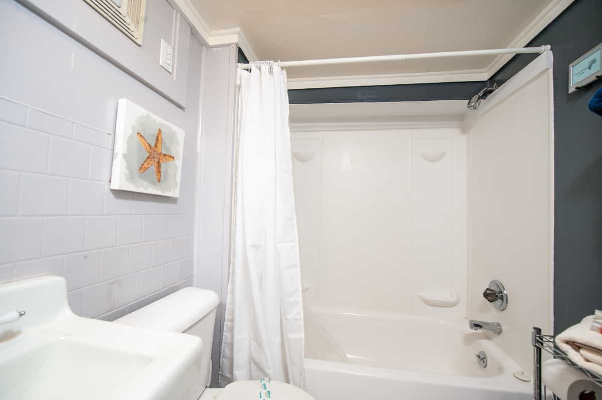 Bright white bathroom with bathtub, shower curtain, sink, and starfish wall art.