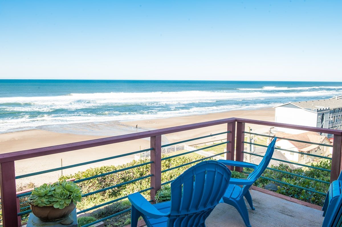 Ocean-view balcony with blue chairs overlooking a sunny beach and waves