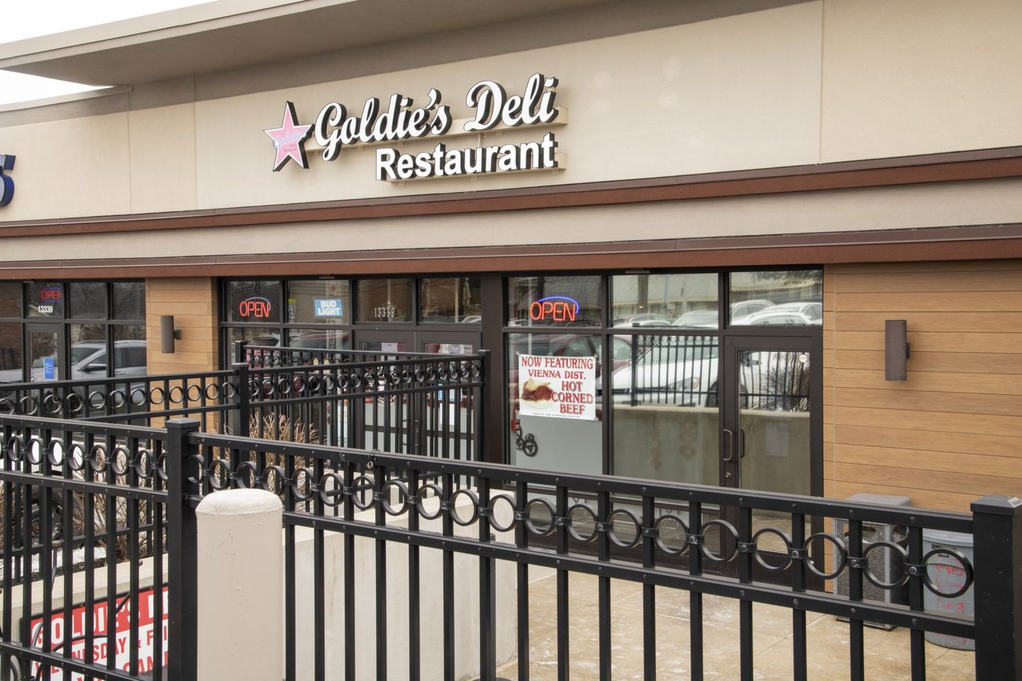 Goldie's Deli Restaurant exterior, black iron fence, glass windows, sign with pink star, tan building.