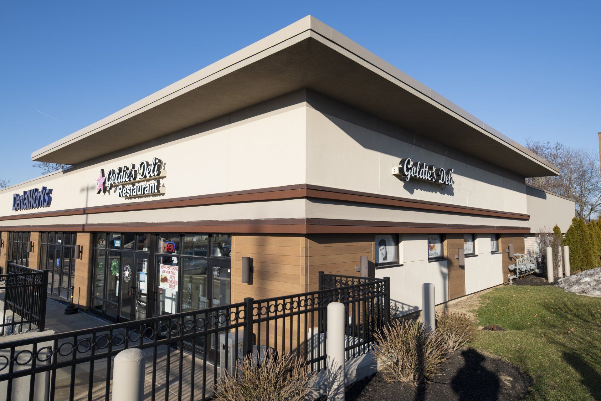 Two-story commercial building with light beige exterior, dark brown accents, and a black wrought-iron fence.