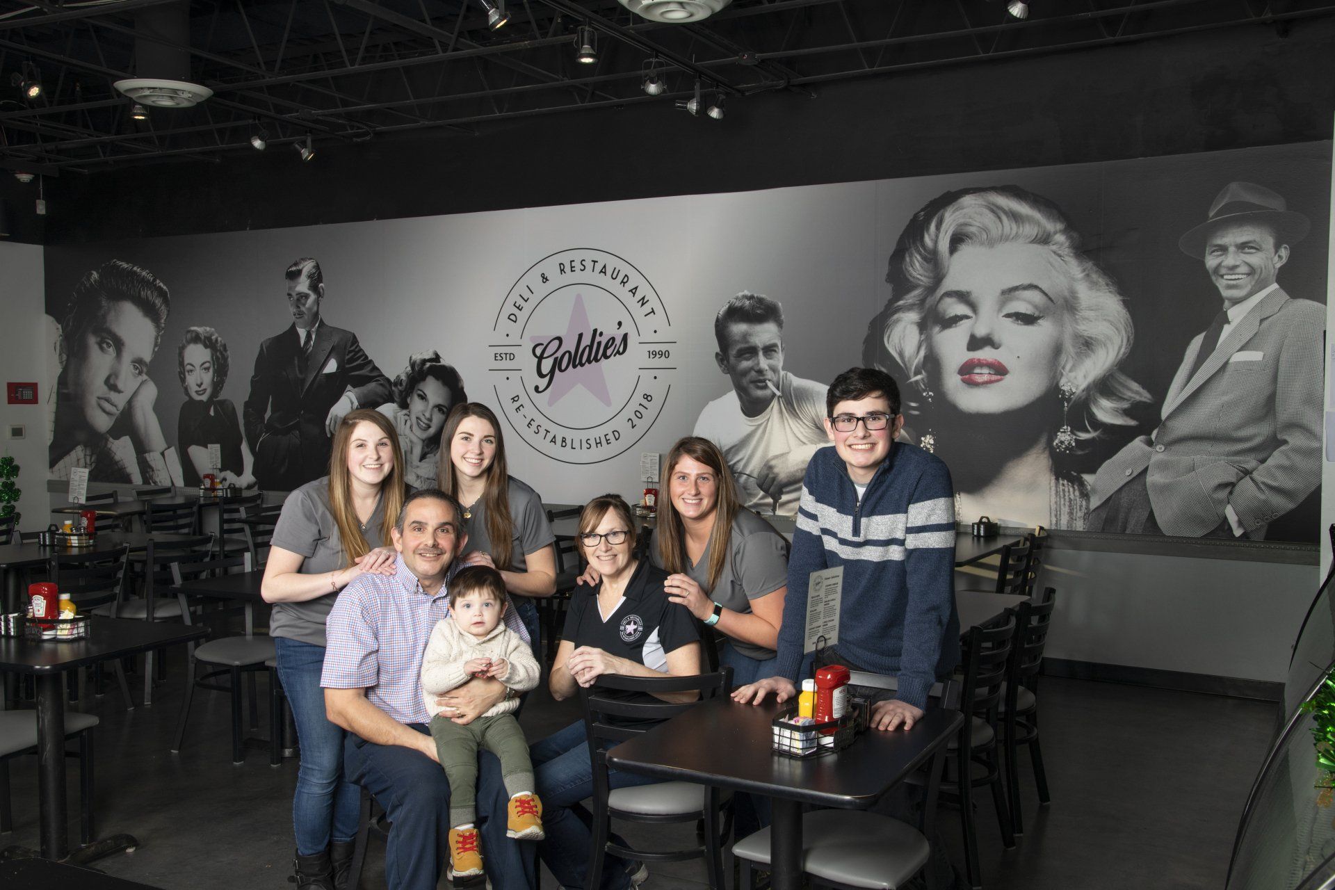 Family poses in front of a restaurant wall mural featuring celebrities.