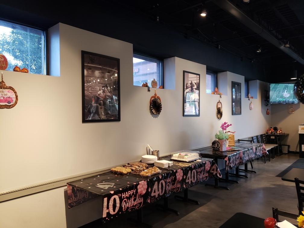 Party room with food tables, decorations, and framed photos under windows.