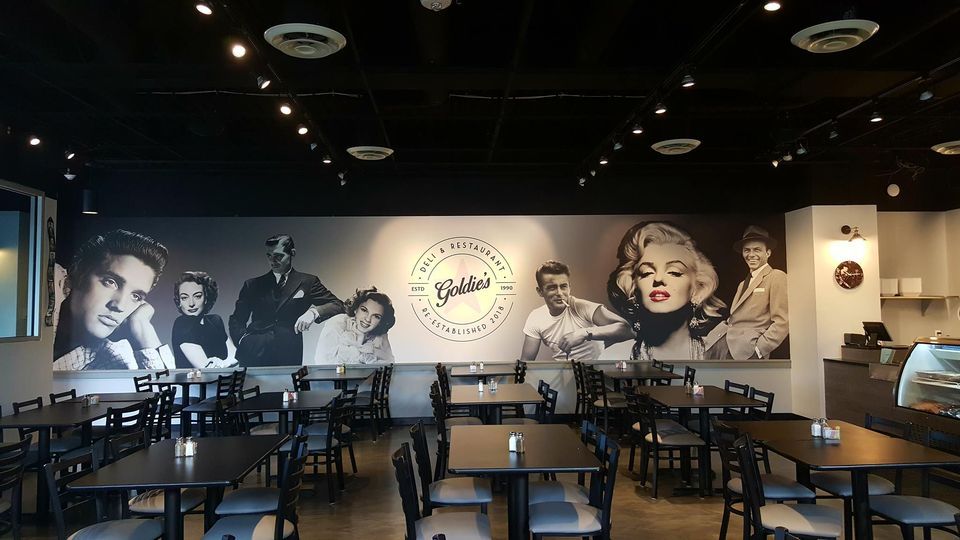 Restaurant interior with black tables and chairs, a mural of classic Hollywood stars.