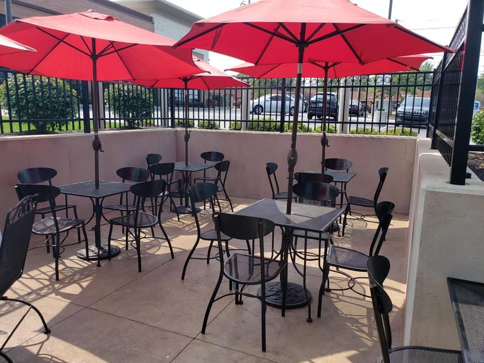 Outdoor seating area with red umbrellas, black tables and chairs, near a black fence.