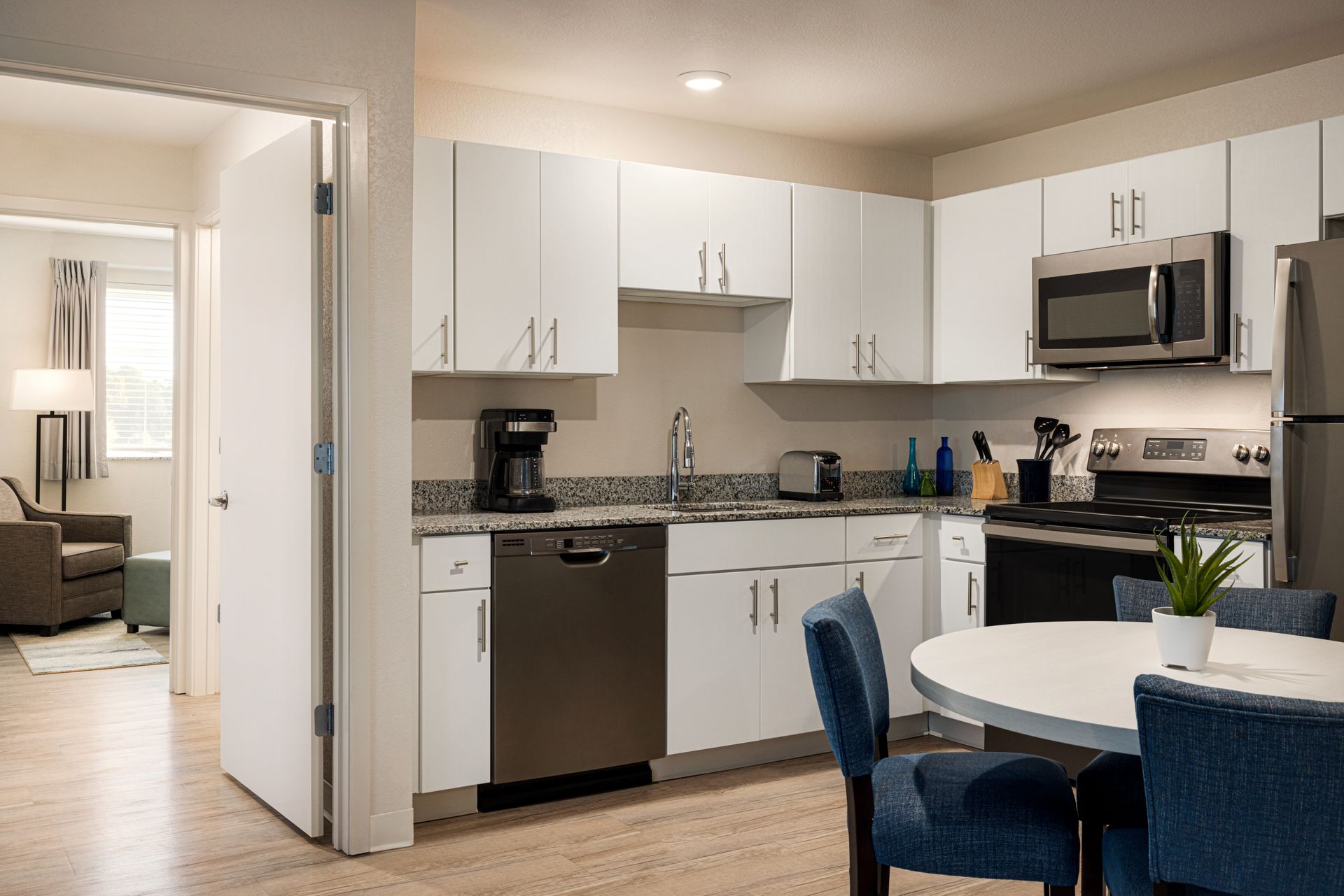A kitchen with white cabinets , stainless steel appliances , a table and chairs.