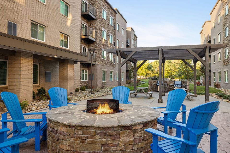 A fire pit surrounded by blue chairs in front of a building.