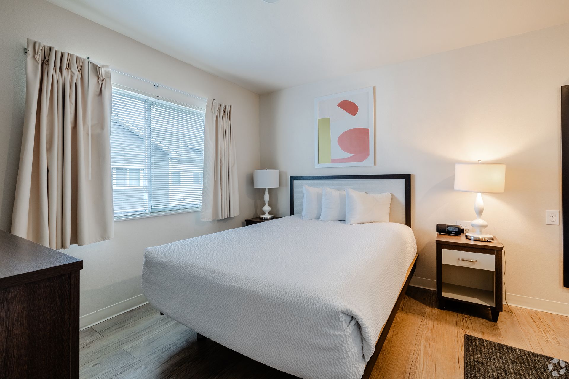 A bedroom with a king size bed , nightstand , lamp and window.