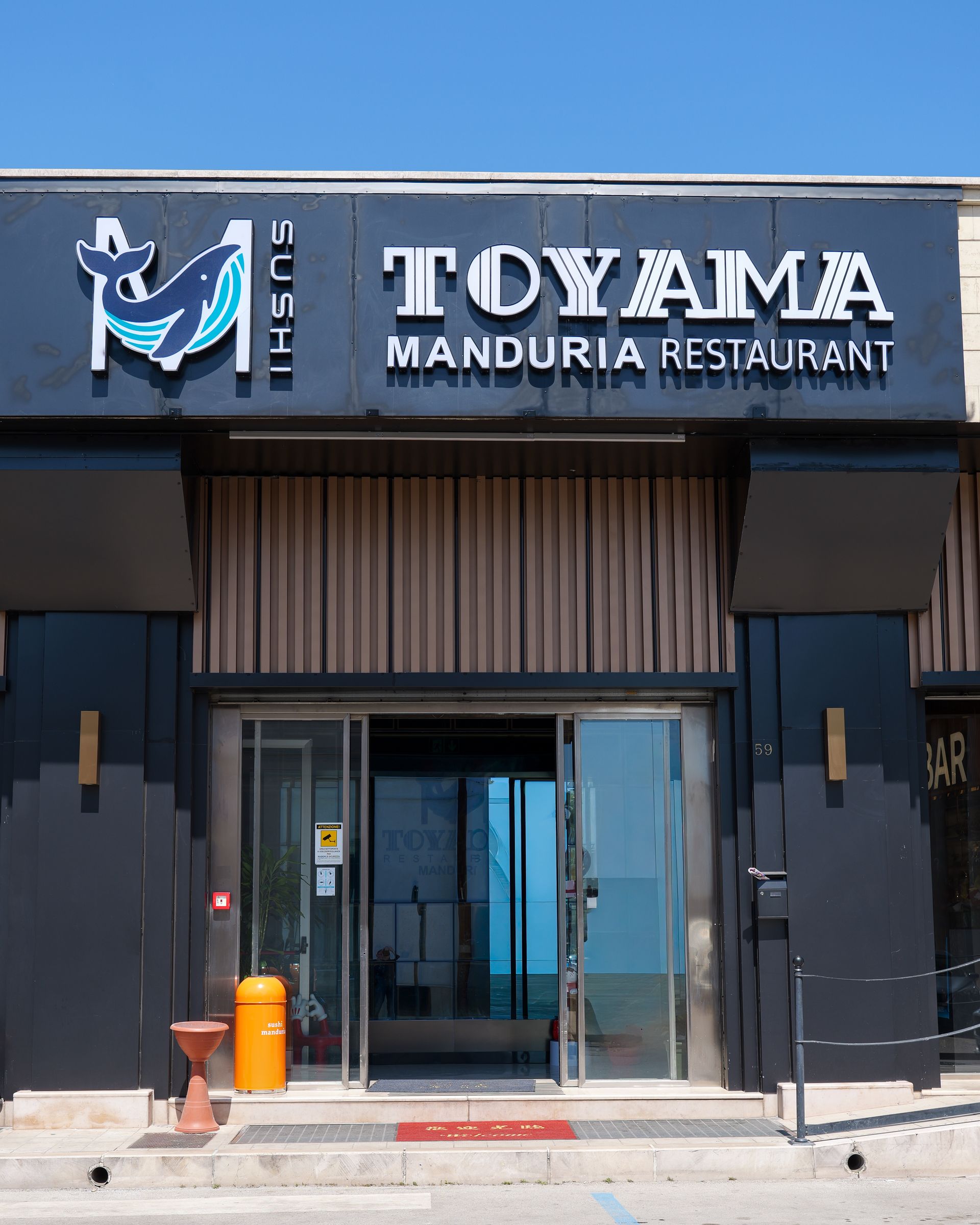 Ingresso del ristorante TQYAM Manduria con facciata nera e porte a vetri.