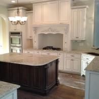 White kitchen with ornate cabinets, marble island, built-in ovens, and dark wood island center