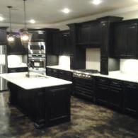 Modern kitchen with dark cabinets, white countertops, and a large island under recessed lights