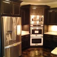 Dark kitchen with stainless steel fridge, built-in oven stack, and dark wood cabinets