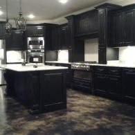 Dark modern kitchen with black cabinets, white countertops, and an island.