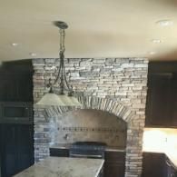 Kitchen with stone arch backsplash, hanging pendant light, and granite island countertops