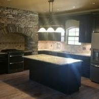 Empty kitchen with stone arch, dark cabinets, central island, and pendant lights