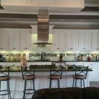 Modern kitchen with bar stools, white cabinets, and a large stainless steel range hood