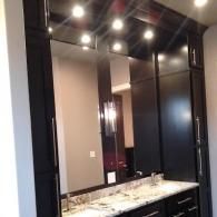 Modern bathroom vanity with marble countertop, large mirror, and dark cabinetry under recessed lights