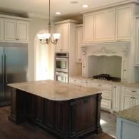 Bright white kitchen with dark island, stainless fridge, built-in oven, and ornate range hood