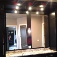 Bathroom vanity with large mirror, dark cabinets, and bright overhead lights.