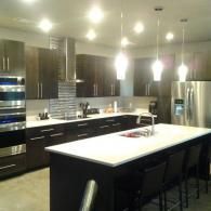 Modern kitchen with dark cabinets, stainless appliances, and a large white island under pendant lights