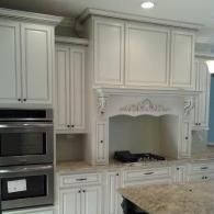 White kitchen with ornate cabinets, built-in oven, and decorative range hood over granite countertop.