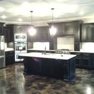 Modern kitchen with dark cabinets, white countertops, and a large island under pendant lights