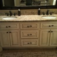 Double vanity bathroom with two sinks, granite countertop, cream cabinets, and decorative tile floor.