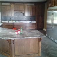 Wooden kitchen with large island, dark cabinets, stainless steel fridge, and a few items on the counter