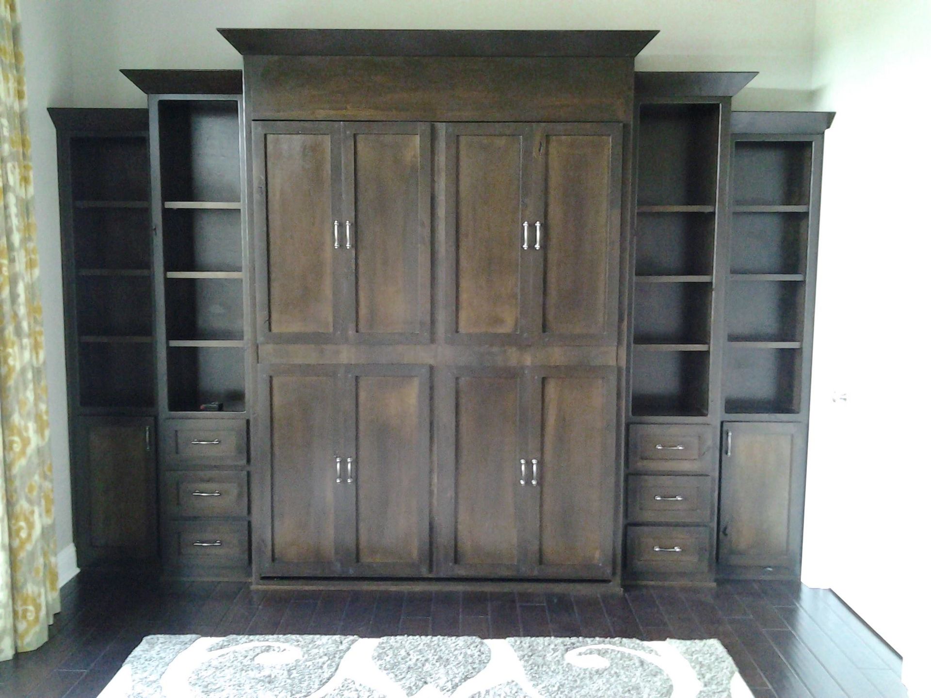 Dark wood built-in wall unit with cabinets, shelves, and drawers in a living room.