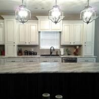 Bright white kitchen with marble island, pendant lights, cabinets, and a window over the sink.