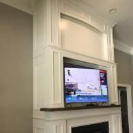Wall-mounted TV in a white built-in cabinet above a fireplace in a living room